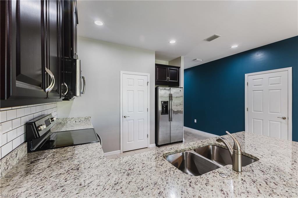 Kitchen with stainless steel appliances, light stone countertops, decorative backsplash, recessed lighting, and dark cabinetry