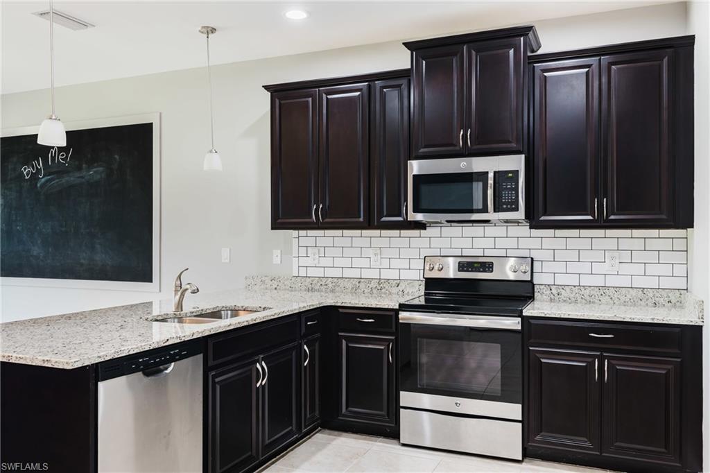 Kitchen with dark cabinets, stainless steel appliances, light stone countertops, a peninsula, and tasteful backsplash
