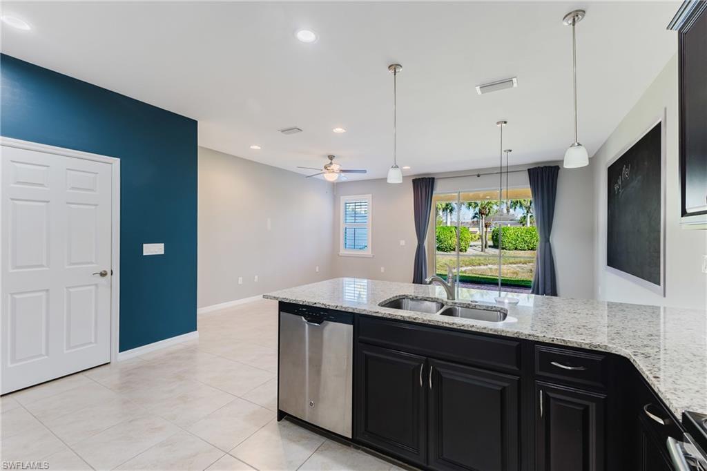 Kitchen featuring dark cabinets, light stone countertops, dishwasher, and hanging light fixtures