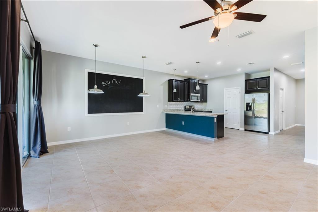 Kitchen with dark cabinetry, stainless steel appliances, open floor plan, a ceiling fan, and pendant lighting