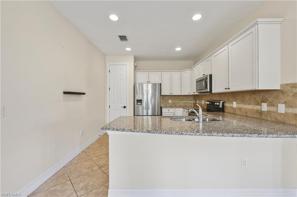 Kitchen featuring white cabinetry, stainless steel appliances, granite countertops, and a tile backsplash