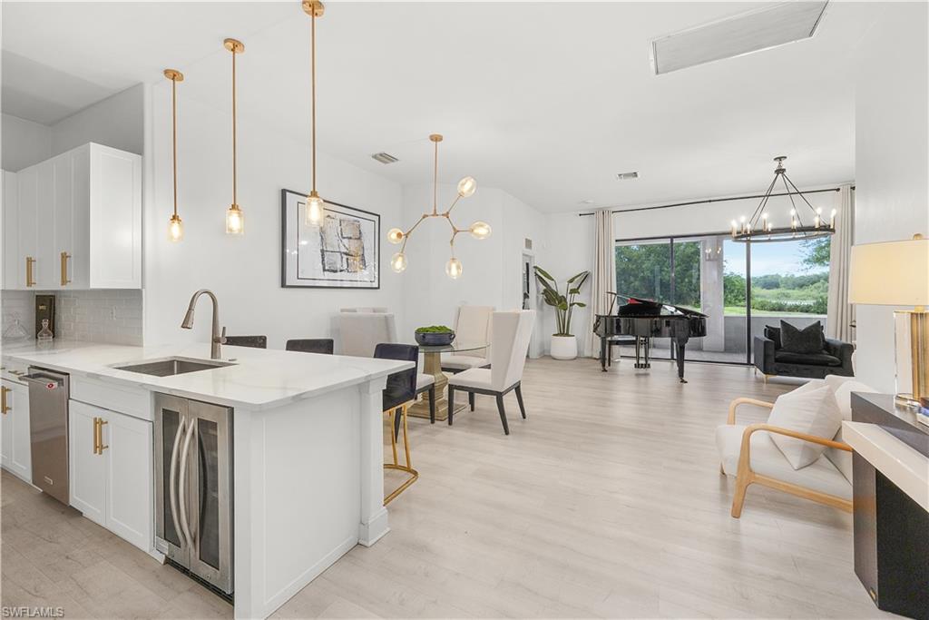 Open-concept living space featuring light wood-finish flooring and a kitchen island with a built-in beverage cooler and stainless steel sink