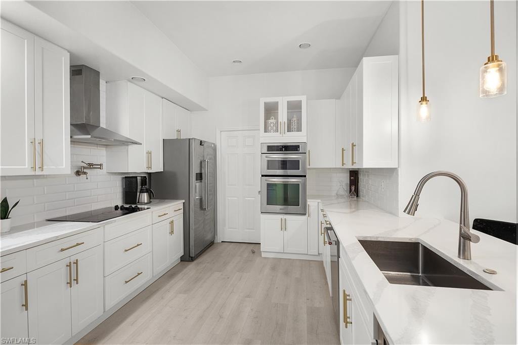 Contemporary kitchen featuring white cabinetry, light-toned wood-finish flooring, stainless steel appliances, a pot filler, and pendant lighting