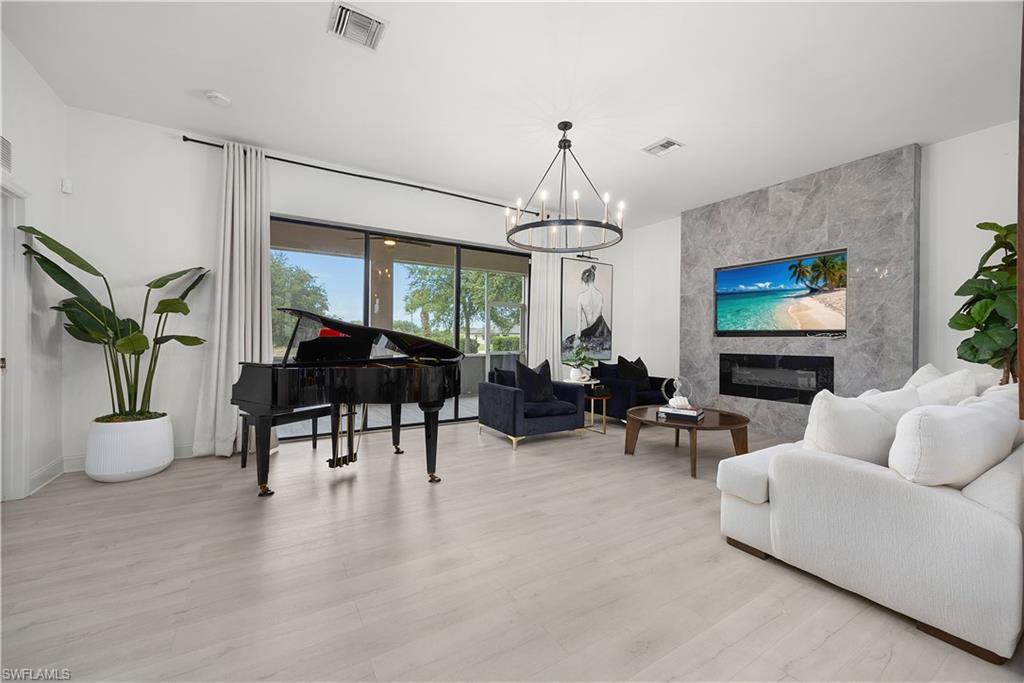 Spacious interior featuring light wood-finish flooring, a contemporary chandelier, and a floor-to-ceiling accent wall with a built-in electric fireplace