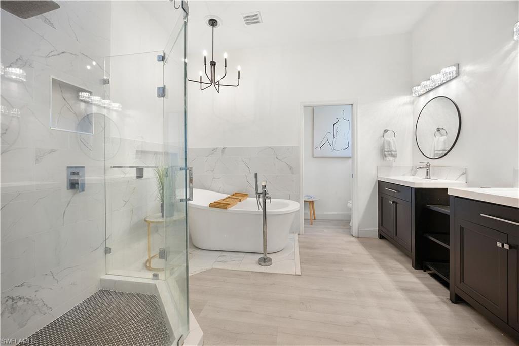 Contemporary bathroom featuring a freestanding soaking tub, clear glass shower enclosure with hex tile flooring, dual dark wood vanities with white countertops, and wood-finish flooring