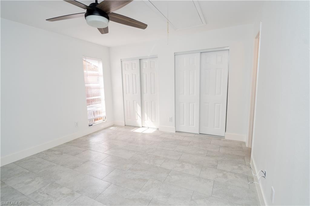 Spacious room featuring light gray tile flooring, a contemporary ceiling fan, and two sets of bi-fold closet doors