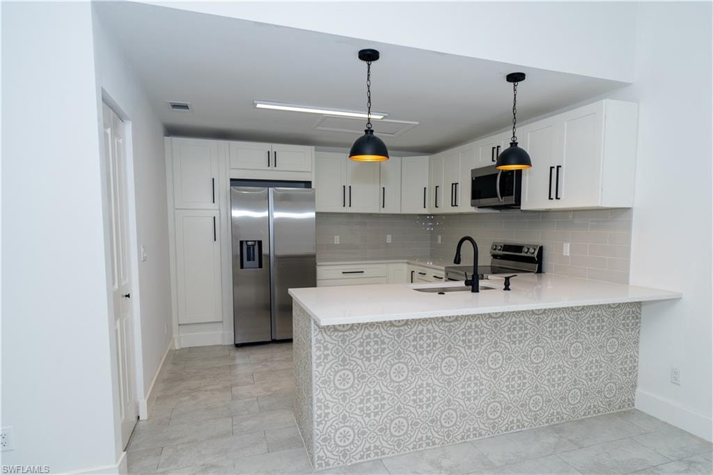 Contemporary kitchen featuring white shaker cabinetry, stainless steel appliances, a subway tile backsplash, and a patterned island facade with a white countertop