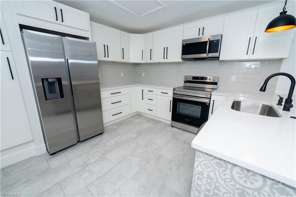 Contemporary kitchen featuring white cabinetry with dark hardware, stainless steel appliances, light subway tile backsplash, and light-toned flooring