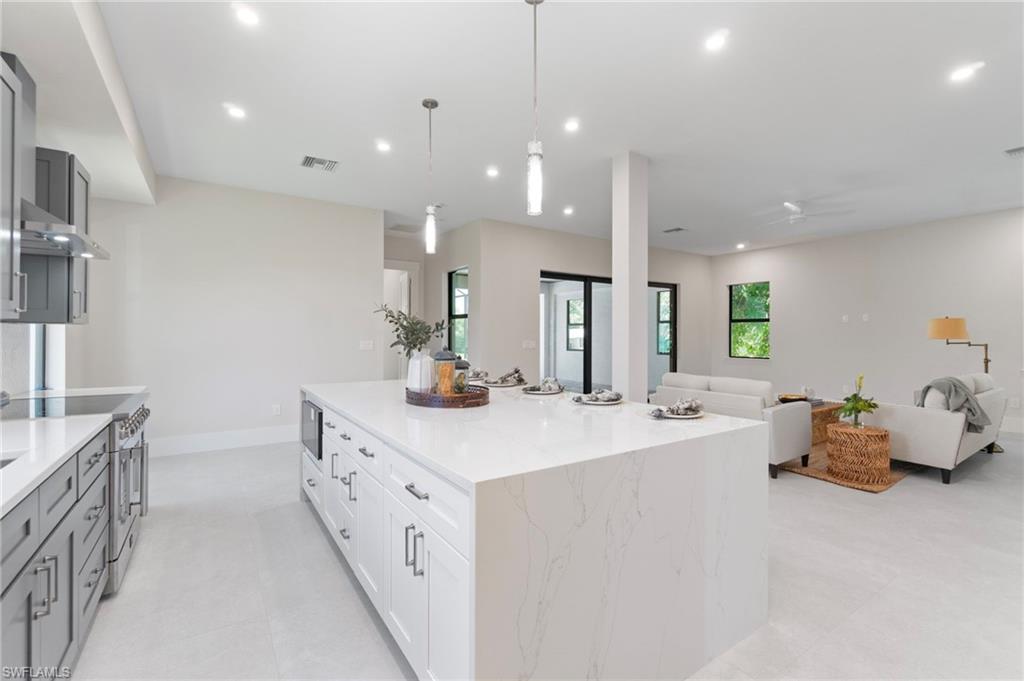 Kitchen featuring white cabinets, a kitchen island, high end stainless steel range, decorative light fixtures, and light stone countertops