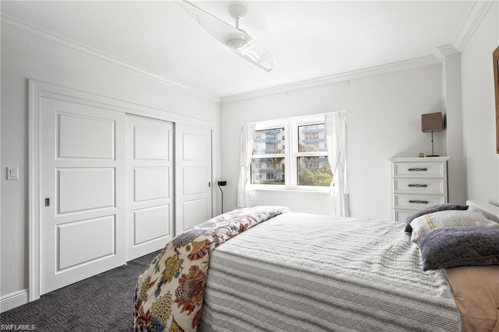 Bedroom featuring ceiling fan, a closet, crown molding, and dark carpet