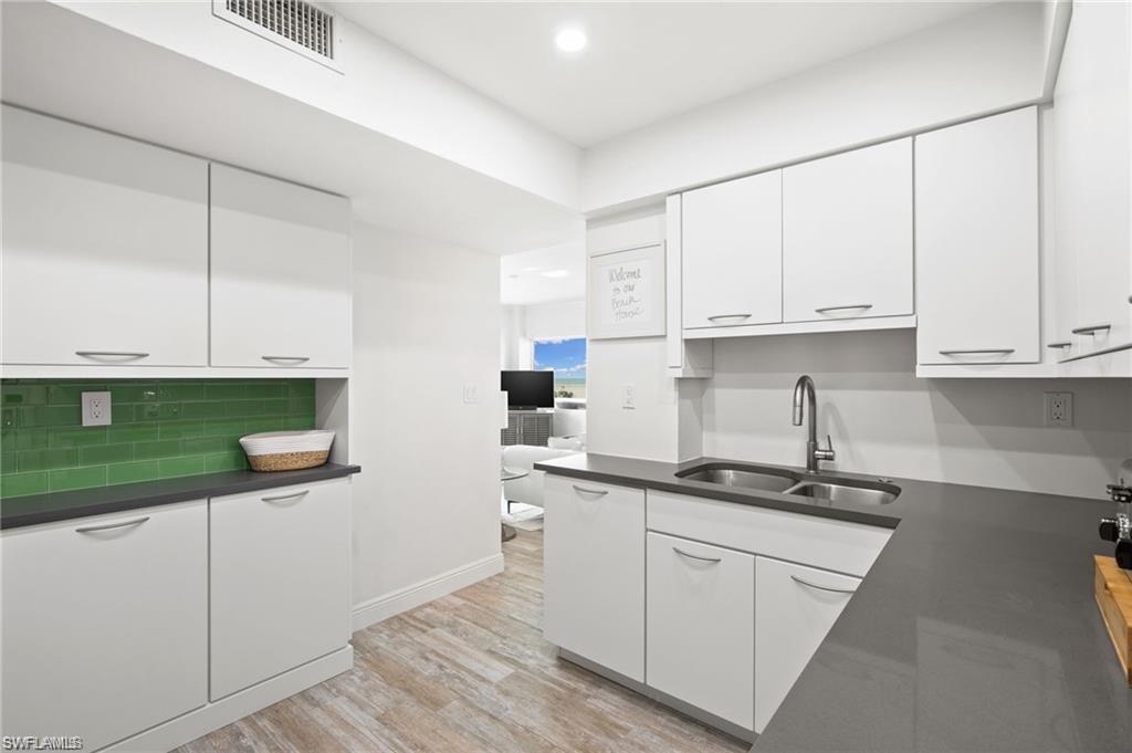 Kitchen with sink, white cabinetry, light hardwood / wood-style flooring, and tasteful backsplash