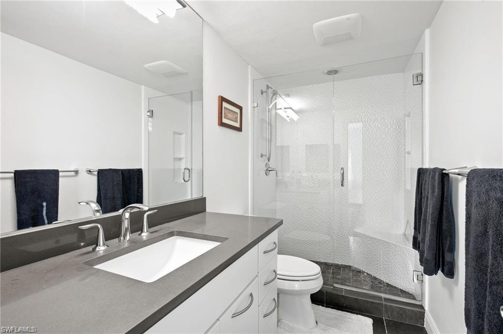 Bathroom with an enclosed shower, oversized vanity, toilet, and tile floors