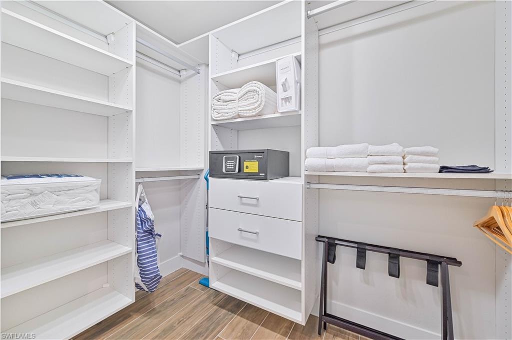 Custom closet system featuring white shelving, multiple hanging rods, integrated drawers with brushed nickel hardware, and wood-finish flooring