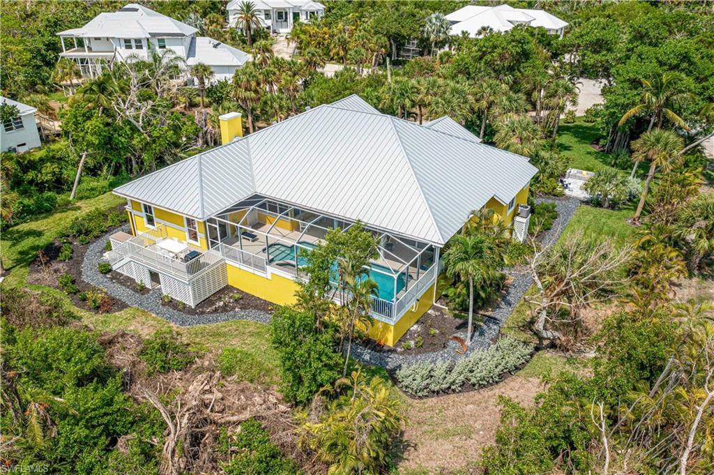 Yellow exterior residence featuring a screened-in pool enclosure, a metal roof, an elevated deck, and surrounding landscaping with mature trees and shrubs