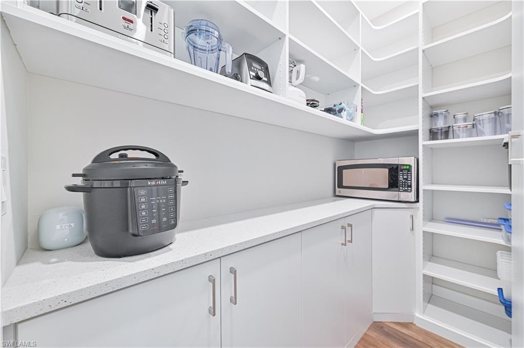 Walk-in pantry featuring extensive white shelving, white perimeter countertops, white cabinetry with silver-tone hardware, and wood-finish flooring
