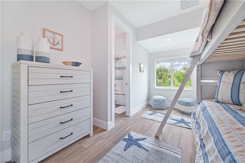 Room featuring wood-finish flooring, a bright window, and an adjacent bathroom with a tiled shower