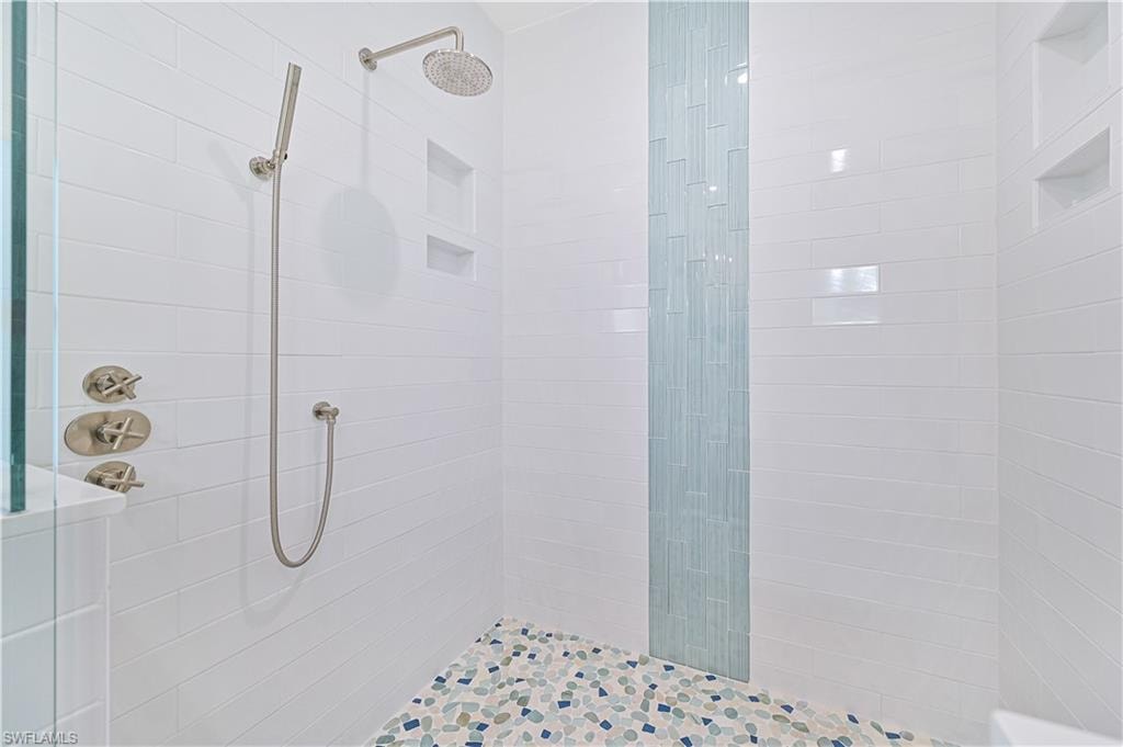 Shower enclosure featuring white subway tile walls, a vertical accent of blue glass tiles, a pebble-finish tiled floor, multiple recessed niches, and brushed nickel fixtures including a rain showerhead and handheld sprayer