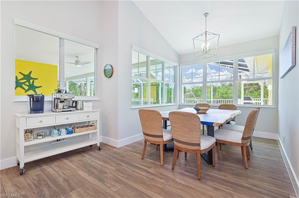 Vaulted ceiling dining area featuring wood-finish flooring, abundant natural light from multiple windows, and a contemporary open-frame chandelier