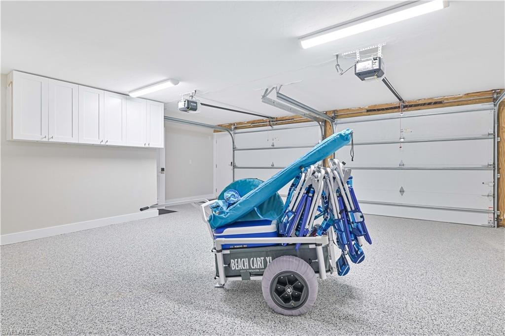 Garage featuring an epoxy-coated floor, bright overhead lighting, white cabinetry, and two overhead door openers
