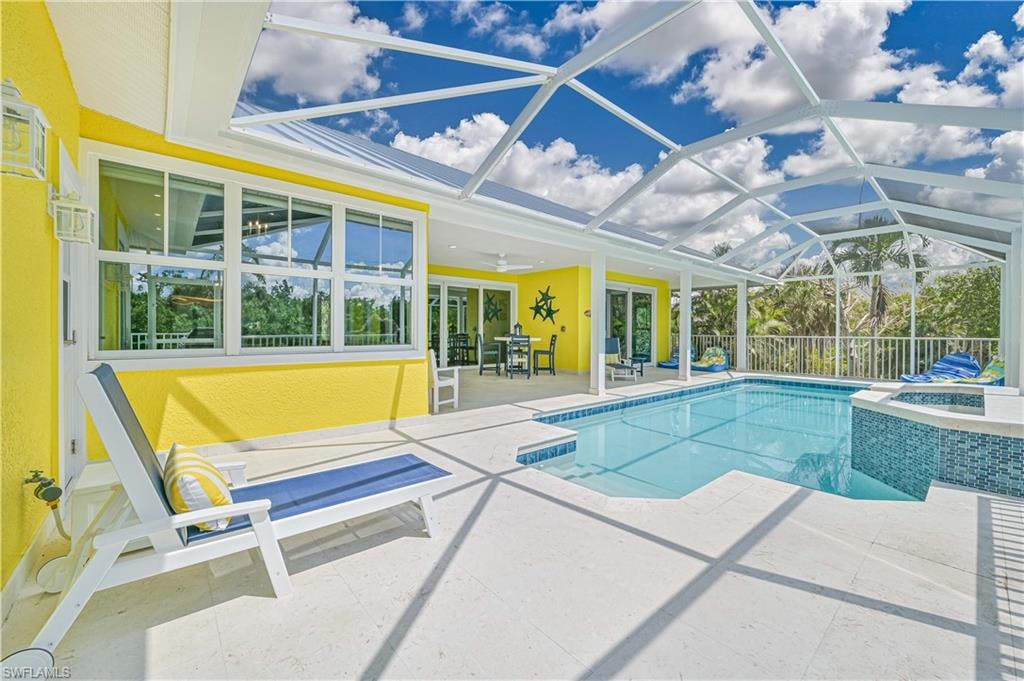 Screened swimming pool and spa area featuring a spacious paver deck, large windows, and sliding glass doors providing access to the interior