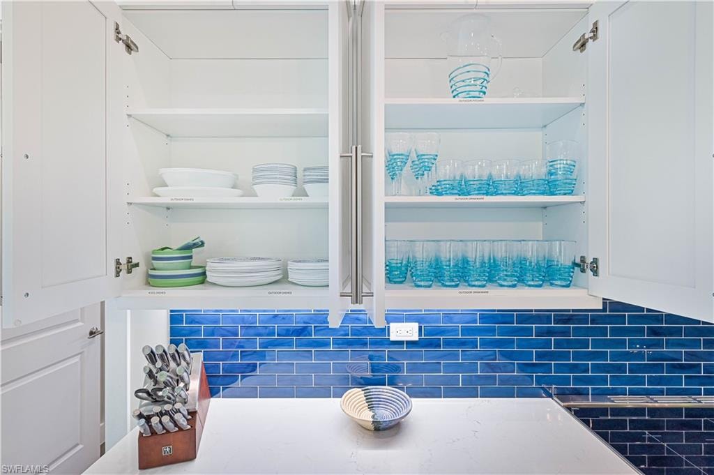 White shaker-style upper cabinetry with interior shelving, under-cabinet lighting, a blue subway tile backsplash, and a light-toned countertop