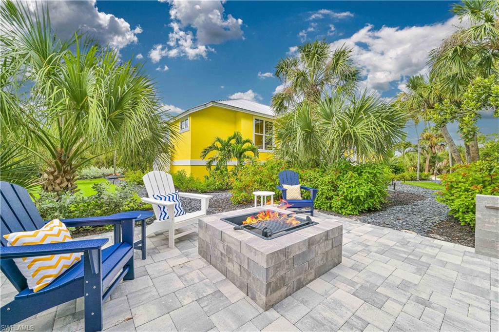 Paver patio featuring a built-in block fire pit, surrounded by lush landscaping and palm trees