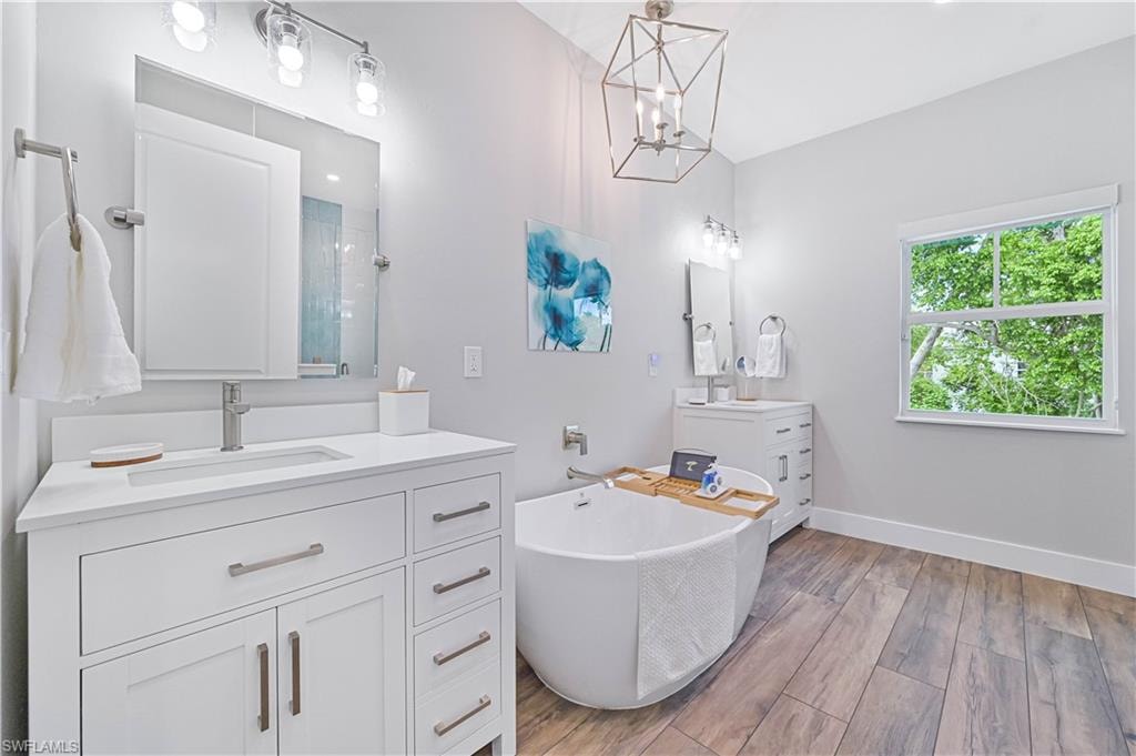 Spacious bathroom featuring wood-finish flooring, a standalone soaking tub, and a dual vanity with white cabinetry and brushed nickel hardware
