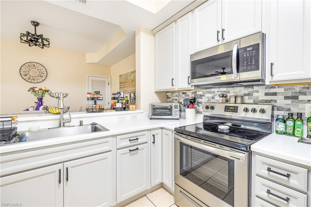 Contemporary kitchen featuring white cabinetry with black hardware, stainless steel appliances, a tile backsplash, and light-toned countertops