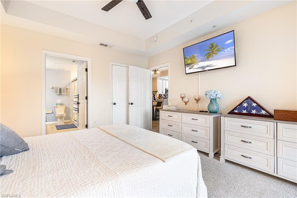 Carpeted bedroom featuring a tray ceiling, ceiling fan, and direct access to a full bathroom