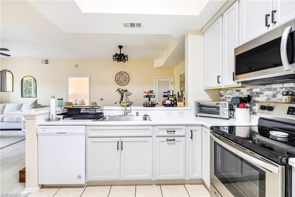 Contemporary kitchen featuring white cabinetry, a light-toned countertop, and stainless steel appliances including a built-in microwave and a range