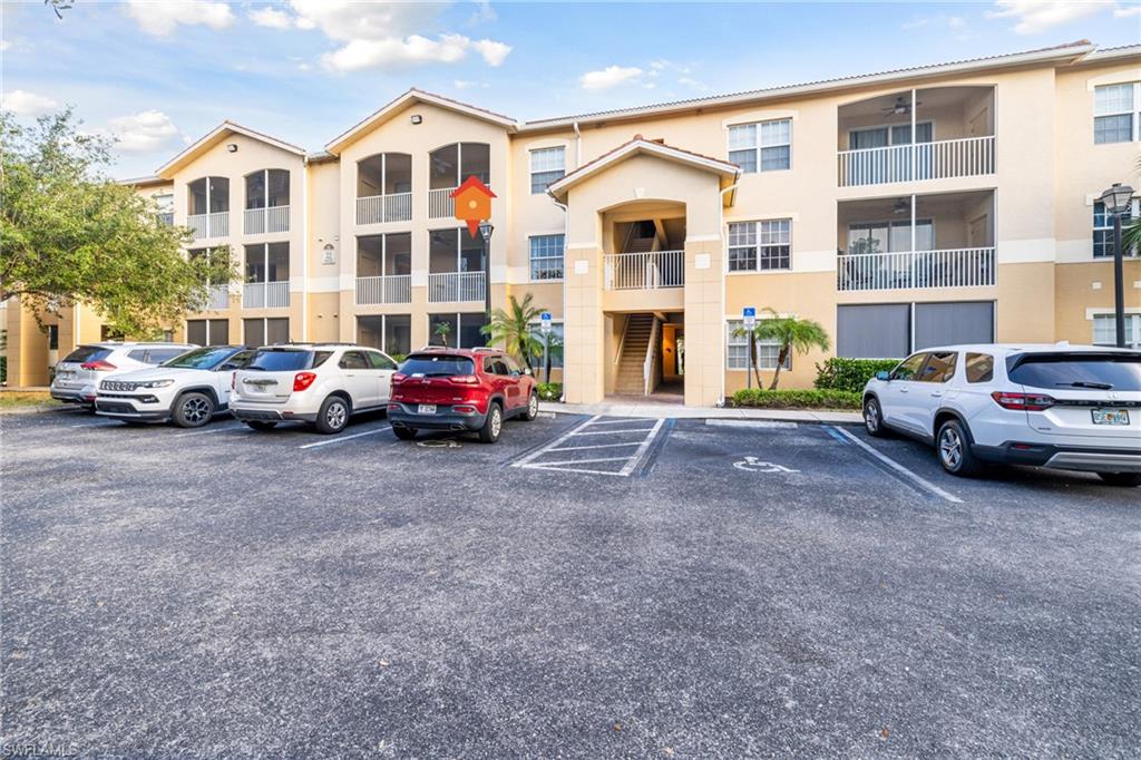 Multi-story residential building featuring screened balconies, an integrated entryway with stairs, and an asphalt parking area with marked spaces