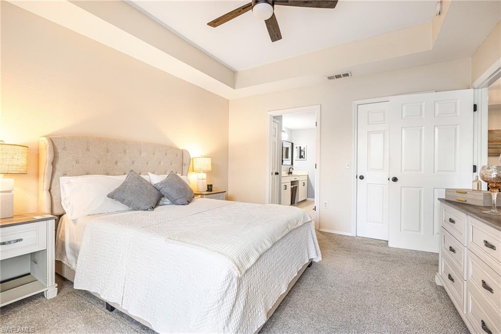 Carpeted bedroom featuring a tray ceiling, ceiling fan, and white paneled doors
