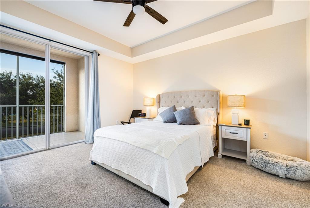Carpeted bedroom featuring a tray ceiling with a ceiling fan, direct access to a balcony through sliding glass doors, and light-toned walls