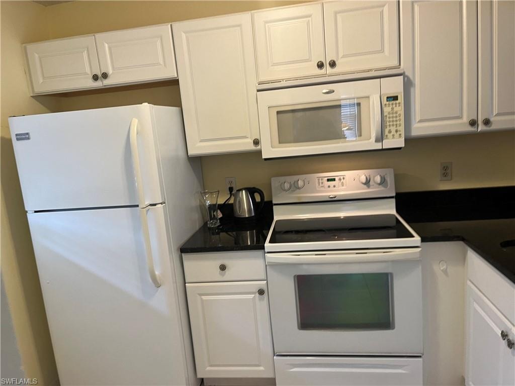 Kitchen with white cabinetry, white appliances, and dark countertops