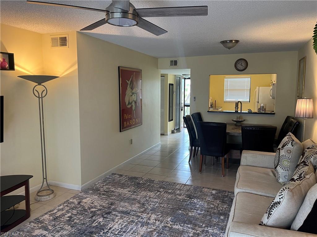 Tiled living area featuring baseboards, visible vents, ceiling fan, and a textured ceiling