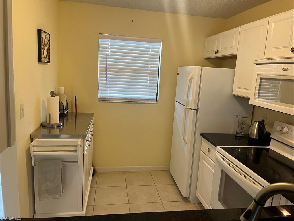 Kitchen with white cabinetry, light tile patterned floors, range, baseboards, and dark countertops