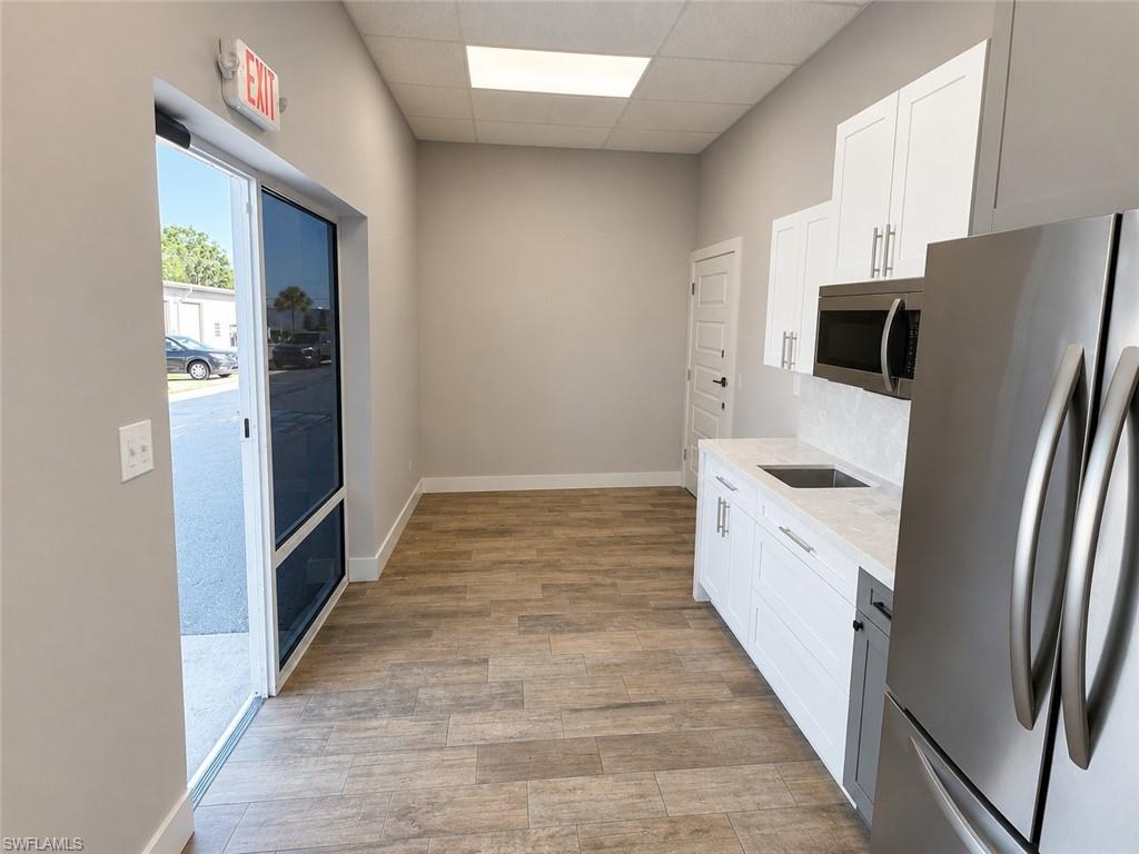 Open concept space featuring wood-finish flooring, white cabinetry, a built-in microwave, and stainless steel refrigerator