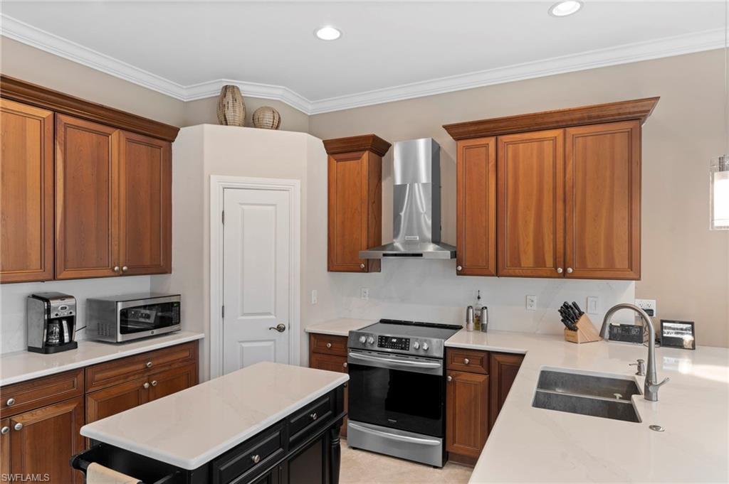 Kitchen featuring light tile patterned flooring, wall chimney exhaust hood, ornamental molding, sink, and appliances with stainless steel finishes