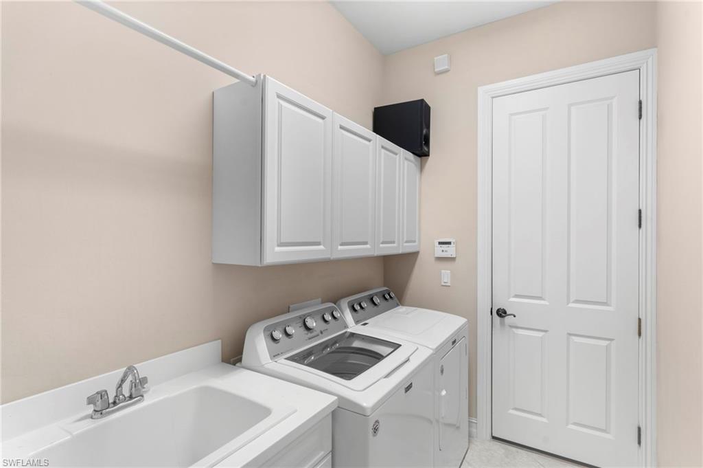 Laundry area with sink, cabinets, light tile patterned floors, and washing machine and clothes dryer