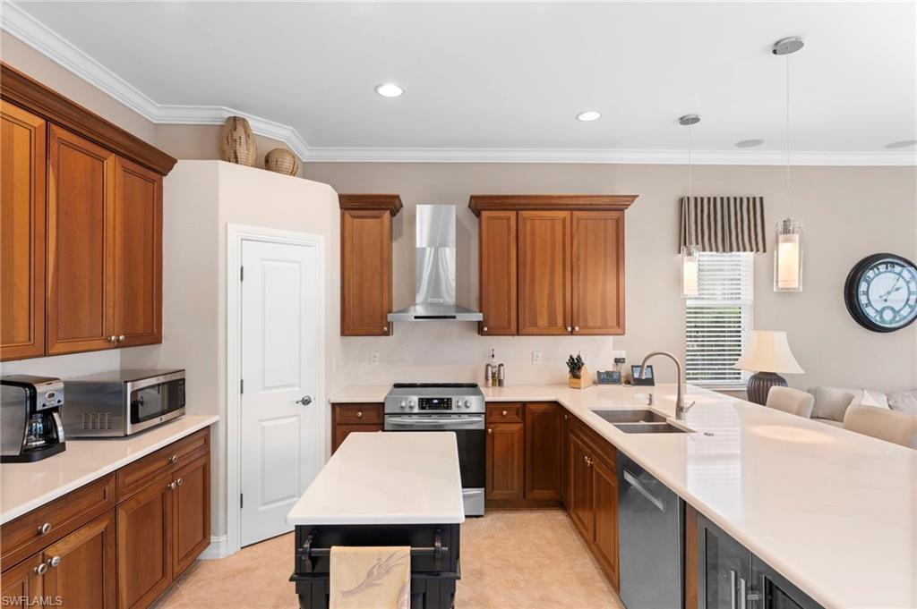 Kitchen featuring stainless steel appliances, sink, hanging light fixtures, wall chimney exhaust hood, and ornamental molding