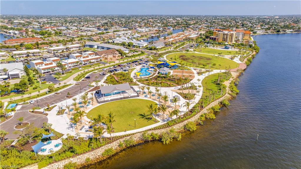 Jaycee Park-Waterfront park featuring expansive green spaces, paved pathways, numerous palm trees, and a community building with a covered patio
