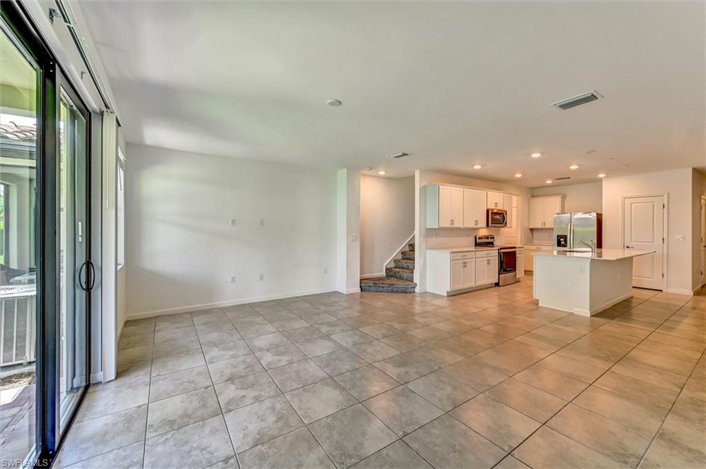 Spacious living room featuring an open floor plan, luxury tile flooring, large windows, and seamless flow into the dining and kitchen areas — a bright and welcoming main living space.