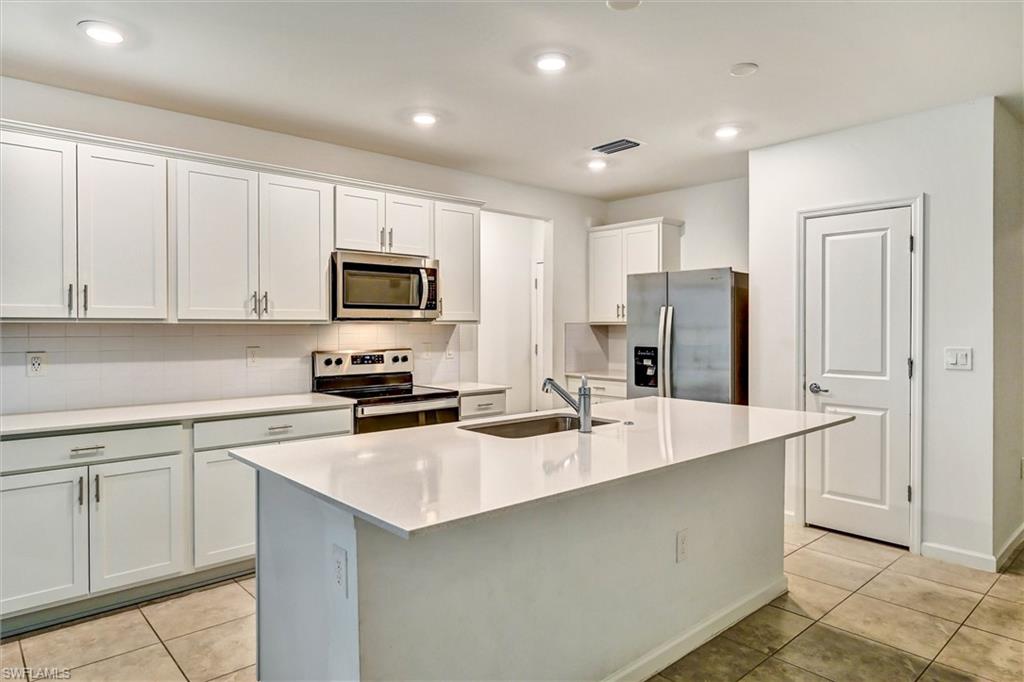 Elegant kitchen with a generous center island, white shaker cabinets, quartz countertops, subway tile backsplash, and premium stainless steel appliances throughout.