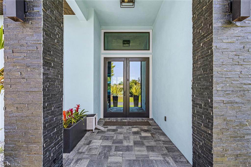 Entryway featuring stacked stone pillars, a double glass-panel door, and a transom window