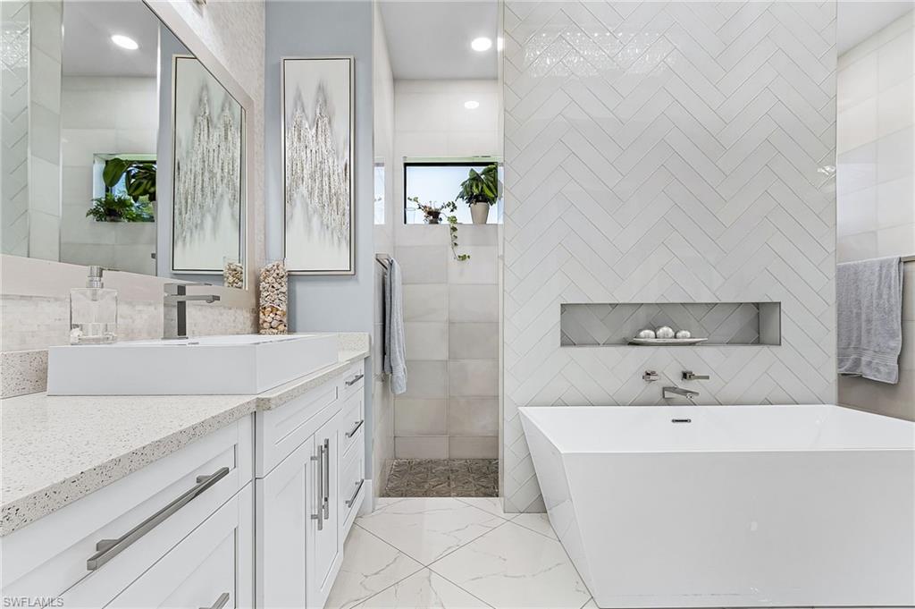 Modern bathroom featuring a freestanding soaking tub with a recessed niche, a walk-in shower with a window, a double vanity with an integrated rectangular sink, and polished chrome fixtures