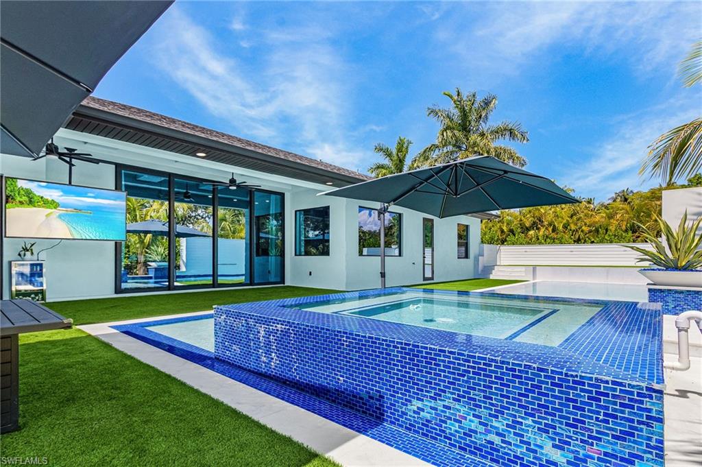 Outdoor space featuring a blue mosaic tiled spa with integrated pool, artificial turf, and a covered patio with an outdoor television