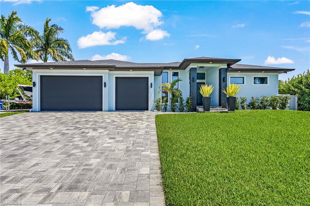 Contemporary exterior featuring a paver driveway, two-car garage, and lush green lawn