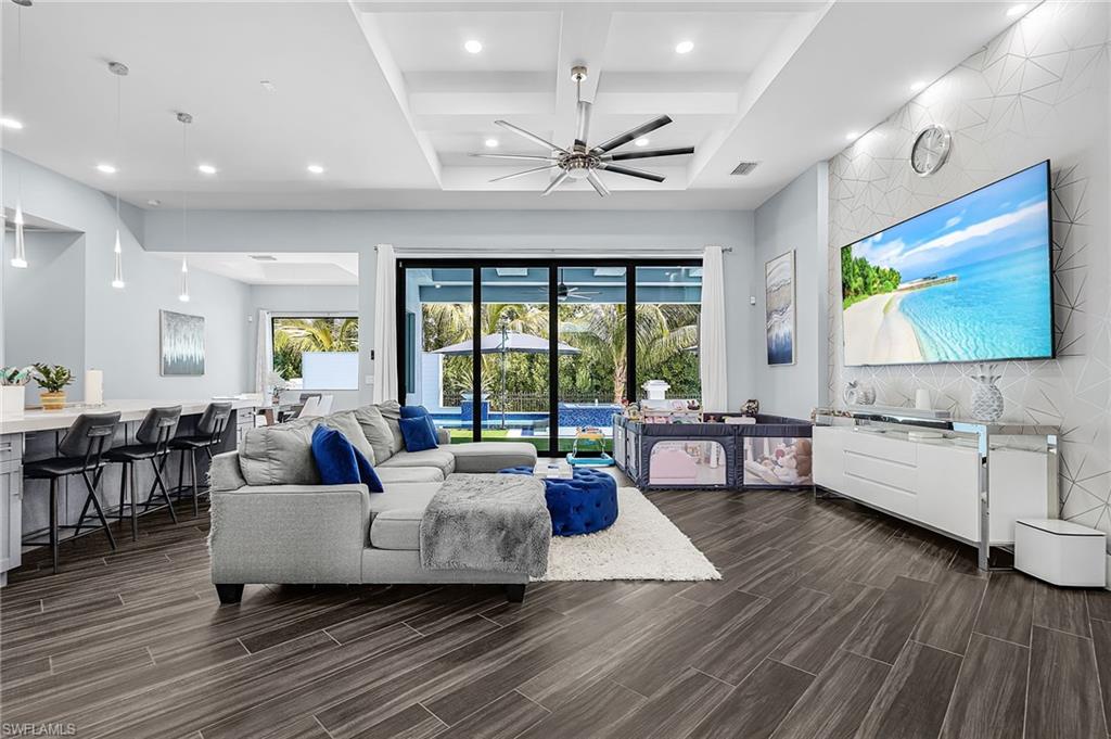 Spacious living area featuring wood-finish flooring, a tray ceiling with a ceiling fan, and recessed lighting