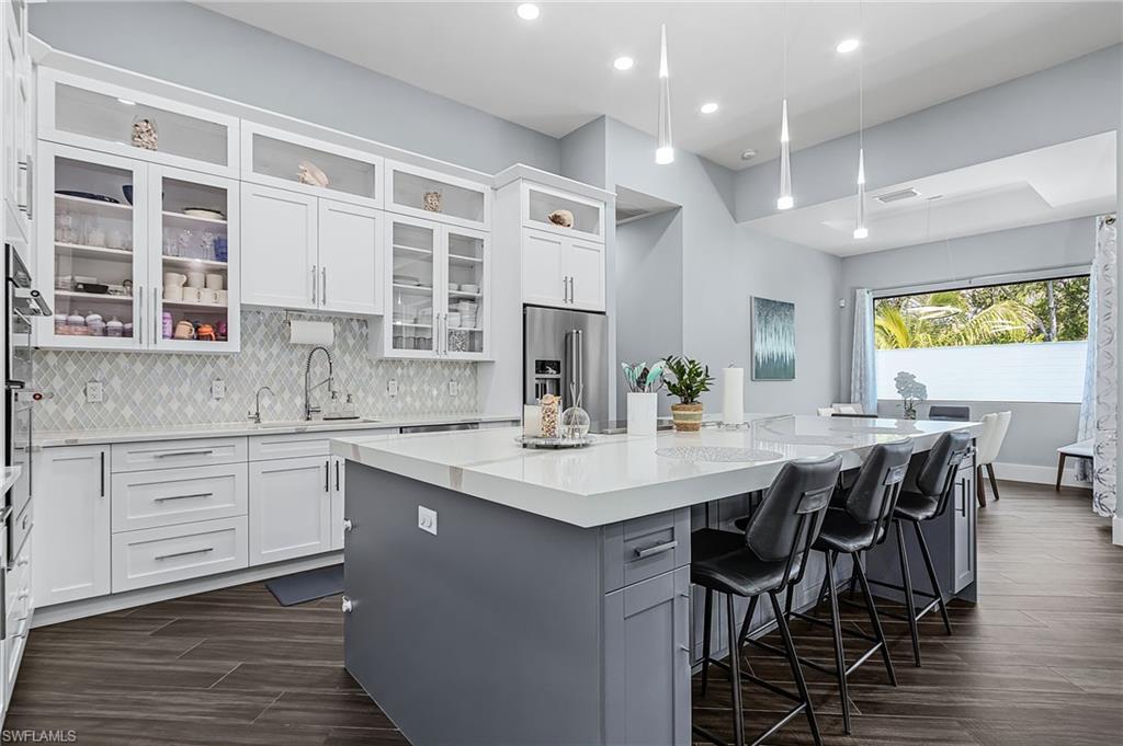 Kitchen featuring a large island with seating, pendant lighting, stainless steel appliances, white cabinetry, and wood-finish flooring