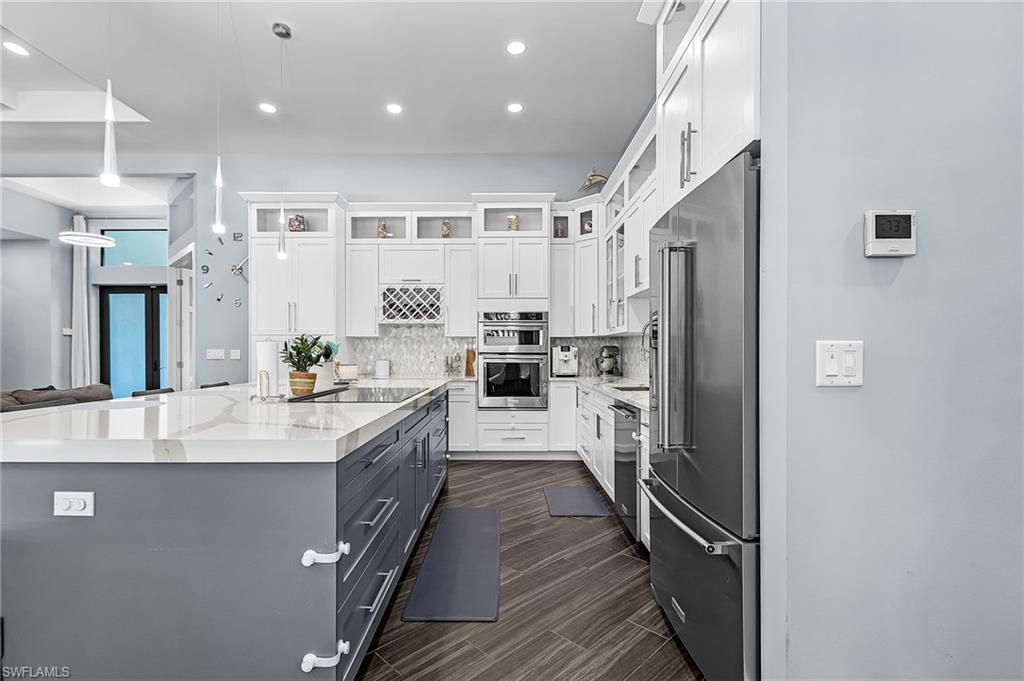 Gourmet kitchen featuring a large central island with a light-toned countertop, stainless steel appliances, white upper cabinetry, gray base cabinetry, and wood-finish flooring